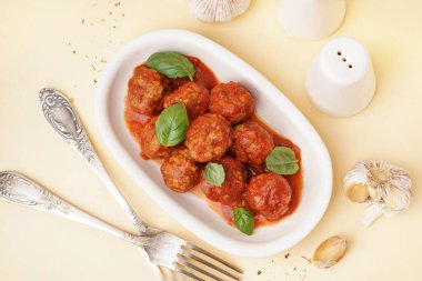 Bir tabak lezzetli köfte, domates sosu ve bej arka planda fesleğen.