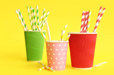 Sarı arka planda farklı pipetli kağıt bardaklar.