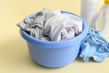 Kirli çamaşırlı plastik leğen ve bej arka planda bir şişe çamaşır deterjanı.
