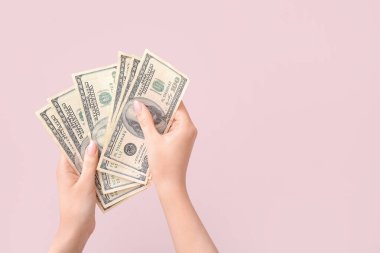 Pembe arka planda 100 dolarlık banknotlar tutan kadın eller.