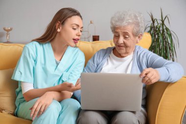 Evde dizüstü bilgisayar kullanan yaşlı bir kadınla ilgilenen kadın.