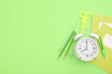 Yeşil arkaplanda farklı kırtasiye malzemesi olan çalar saat