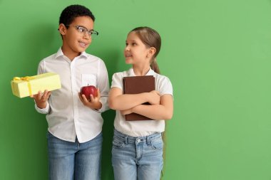Yeşil arka planda kitabı, hediyesi ve elması olan küçük öğrenciler