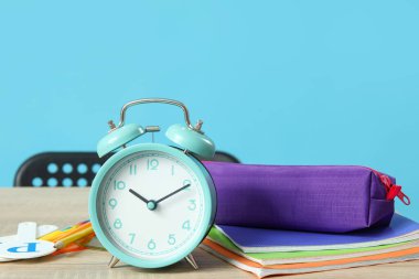 Mavi arka planda alarm saati ve kırtasiyesi olan modern okul masası