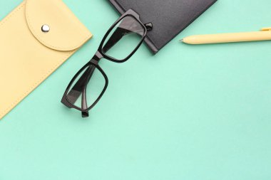Şık gözlüklü kompozisyon, çanta ve turkuaz arka plan üzerine not defteri.
