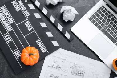 Laptop with clapperboard, storyboard and pumpkins on grunge grey background. Halloween celebration clipart