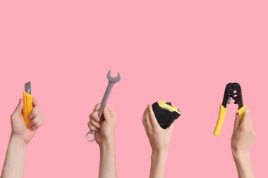 Electrician hands with tools on pink background