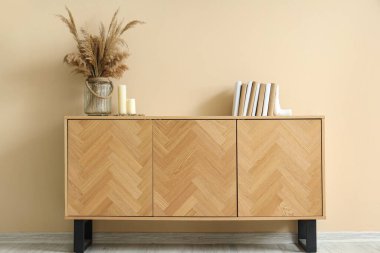 Kitaplar, mumlar ve vazolar. Odadaki bej duvarın yanındaki çekmecelerde otlar var.