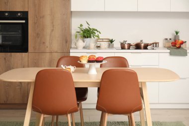 Muffinler ve tarçınlı rulolarla birlikte ahşap mutfak masasında durun.