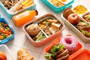 Farklı lezzetli yemekleri olan bir sürü beslenme çantası ve beyaz fayanslı bir şişe meyve suyu.