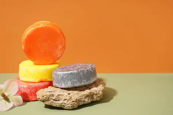 stock image Solid colorful shampoo bars with stone and flower on green table orange wall