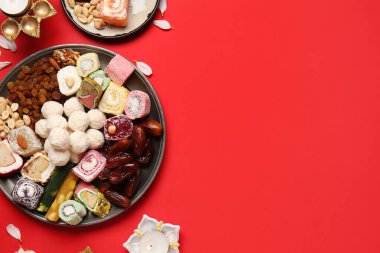 Kırmızı zemin üzerinde mum ve farklı tabaklar bulunan Diya lambaları. Divaly kutlaması