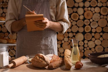 Pastanedeki masada defteri ve taze ekmeği olan genç adam.