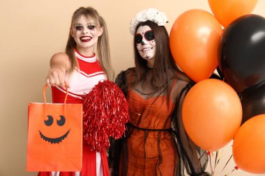 Cadılar Bayramı için giyinmiş bayan arkadaşlar hediye çantası ve bej arka planda balonlar.