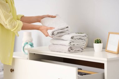 Bir kadın evdeki çekmecelerin üzerine kıyafet yığıyor, yakın plan.