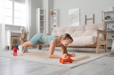 Evde yoga minderinde egzersiz yapan genç bir kadın fitness eğitmeni.