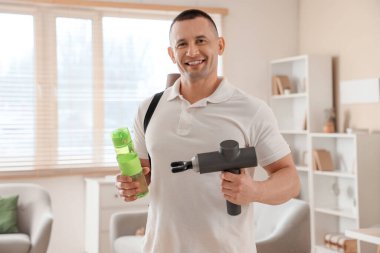 Evde vurmalı masaj aleti ve su şişesi olan genç bir adam.