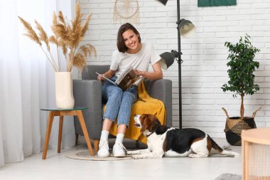 Kitap okuyan genç bir kadın ve evde yerde yatan sevimli bir Beagle köpeği.