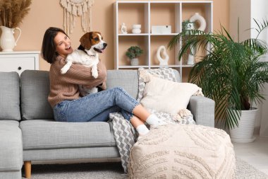 Evdeki rahat kanepede sevimli Beagle köpeğine sarılan genç bir kadın.