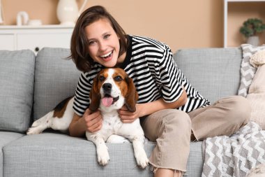 Genç bir kadın evdeki rahat kanepede sevimli Beagle köpeğine sarılıyor.