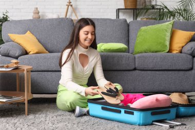 Evde yerde parmak arası terlikleri bavulda toplayan genç bir kadın. Yaz yolculuğu konsepti