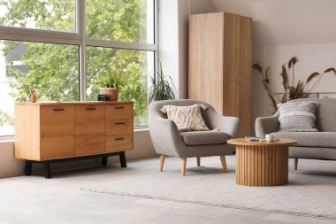 Gri kanepesi, koltuğu ve ahşap çekmeceleri olan açık renk oturma odası.