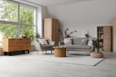 Gri kanepesi, koltuğu ve ahşap çekmeceleri olan açık renk oturma odası.