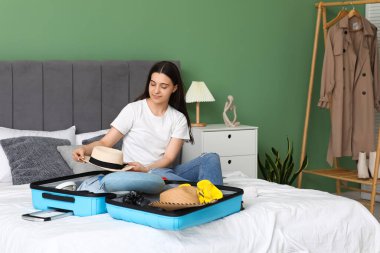 Evdeki yatakta bavulunu toplayan genç bir kadın. Yaz yolculuğu konsepti