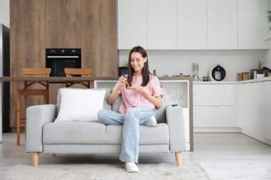 Şeker hastası genç bir kadın mutfaktaki kanepede tükenmez kalem kullanıyor.