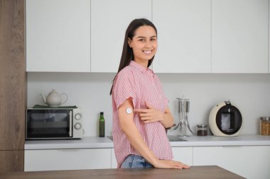 Mutfakta şeker hastası genç bir kadın glikoz sensörünü işaret ediyor.