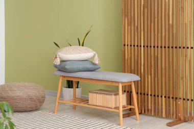 Oturma odasında rahat bir bank, ev bitkisi, yastıklar ve katlanır ekran var.