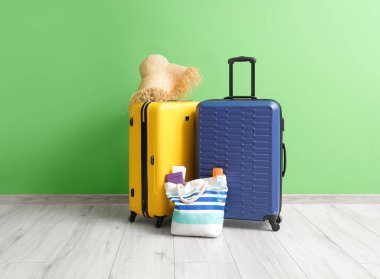 Hasır şapkalı bavullar ve yeşil duvarın yanında pasaportlu plaj çantası.