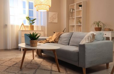 Kanepesi, koltuğu, sehpası, dizüstü bilgisayarı ve parlak lambaları olan modern oturma odasının güzel iç mekanı.