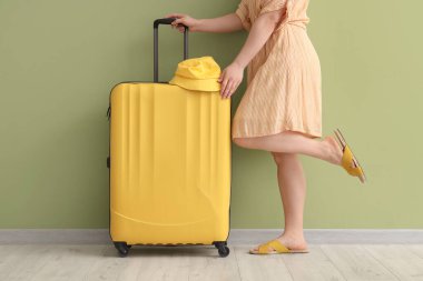 Yeşil arka planda bavulu ve Panama şapkası olan genç bir kadın.