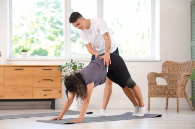 Genç adam evde yoga pozisyonunda kız arkadaşına yardım ediyor.