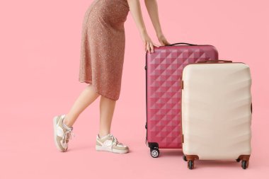 Pembe arka planda bavulları olan genç bir kadın.