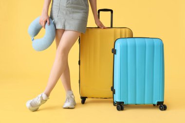 Sarı arka planda bavulları ve boyun yastığı olan genç bir kadın.