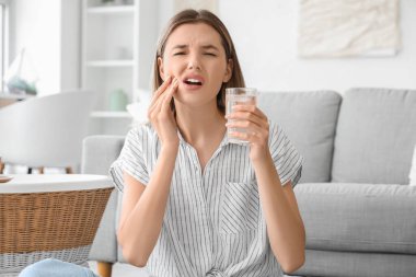 Bir bardak soğuk suyla evde diş ağrısı çeken genç bir kadın.