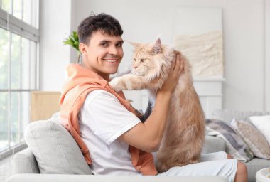 Evdeki kanepede oturan sevimli Maine Coon kedisi olan yakışıklı genç adam.