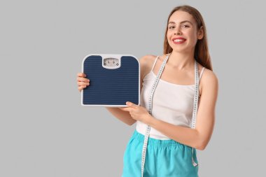 Gri arka planda mezura ve pulları olan sportif genç bir kadın. Kilo verme konsepti