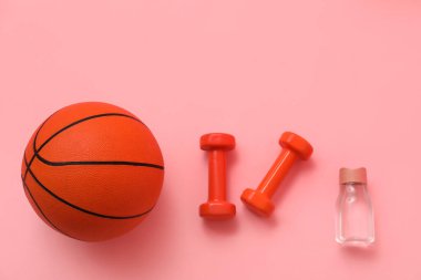Basketbol topu, halterler ve pembe arka planda bir şişe su.
