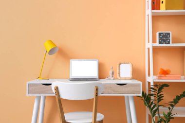 Turuncu duvarın yanında modern dizüstü bilgisayarı olan rahat bir çalışma alanı