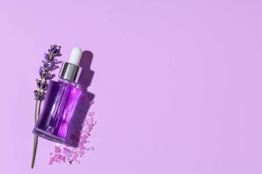 Bir şişe lavanta yağı, çiçekler ve leylak arka planda deniz tuzu.