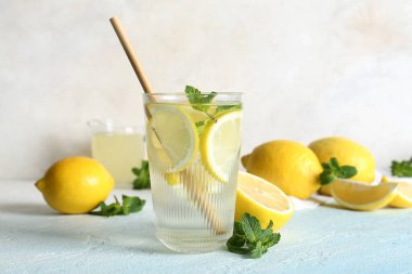 Bir bardak taze limonata, nane ve açık mavi masada meyveler.