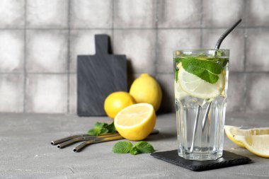 Bir bardak taze limonata, nane ve gri masada meyveler.