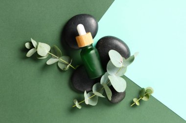 Renkli arka planda spa taşları ve bir şişe okaliptüs esaslı yağ, yakın plan.