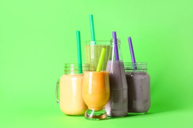 Yeşil arka planda farklı taze meyve suyu kavanozları ve bardaklar.