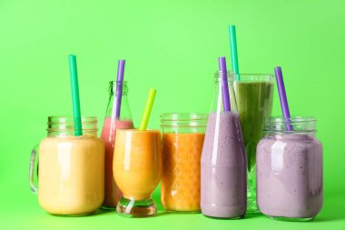 Yeşil arka planda farklı taze meyve suyu kadehleri ve şişeleri.