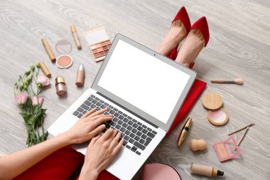 Kozmetik ürünleriyle makyaj sanatçısı ahşap zeminde dizüstü bilgisayar kullanıyor, yakın plan.