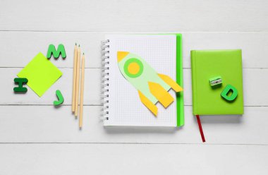 Kalemli kâğıt roket ve beyaz ahşap arka planda farklı kırtasiye malzemeleri. Üst görünüm